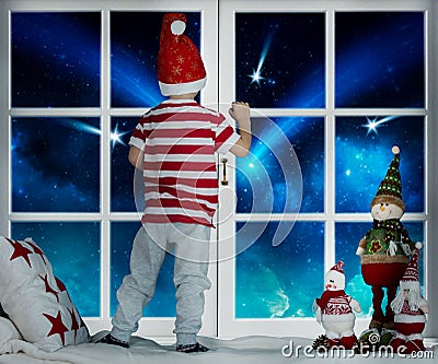 Merry Christmas and happy holidays! Little child boy stands on the window and looking starfall. Room decorated on Christmas. Kid e Stock Photo