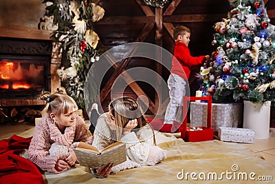 Merry Christmas and Happy New Year. Beautiful family in Xmas interior. Pretty young mother reading a book to her Stock Photo