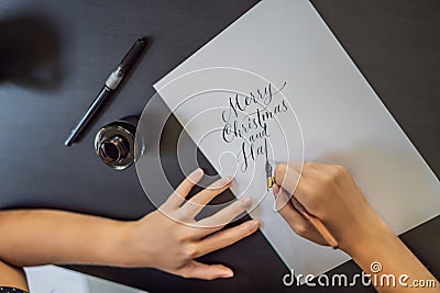 Merry christmas and a happy new year. Calligrapher Young Woman writes phrase on white paper. Inscribing ornamental Stock Photo