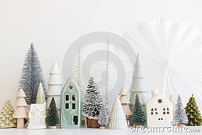 Merry Christmas! Stylish little Christmas trees and house decorations on white table. Modern christmas scene, miniature snowy Stock Photo