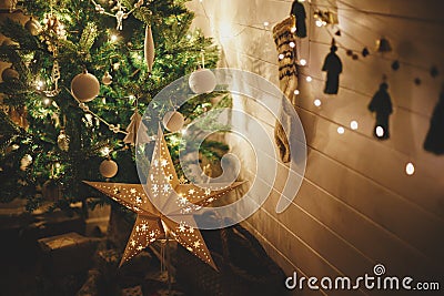 Merry Christmas! Stylish Christmas star, tree with white baubles, boho ornaments, golden lights and gifts in atmospheric evening Stock Photo