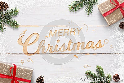 Merry Christmas text hand carved in white woodej surface surrounded with Christmas gifts, fir branches and pinecones Stock Photo