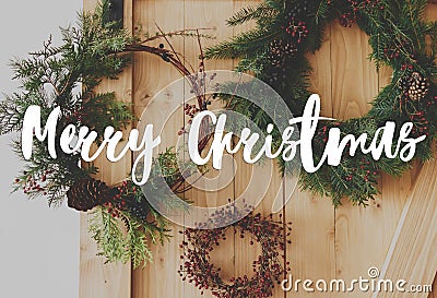 Merry Christmas text handwritten on creative different christmas wreaths hanging on stylish rural door. Greeting card, modern Stock Photo