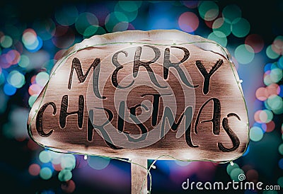 Merry Christmas wooden sign illuminated with holiday lights against a backdrop of Christmas trees adorned with festive lights Stock Photo