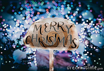 Merry Christmas wooden sign illuminated with holiday lights against a backdrop of Christmas trees adorned with festive lights Stock Photo