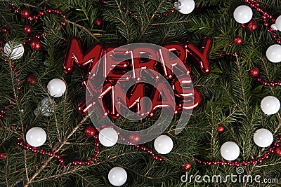 merry xmas written on a glossy red plastic wall decoration placed on a pile of fir branches Stock Photo
