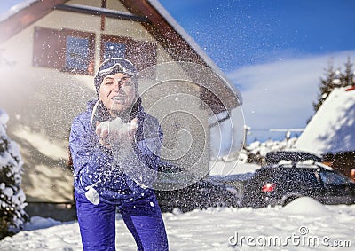 Merry young female blows snow into camera on the cute mountain house background Stock Photo