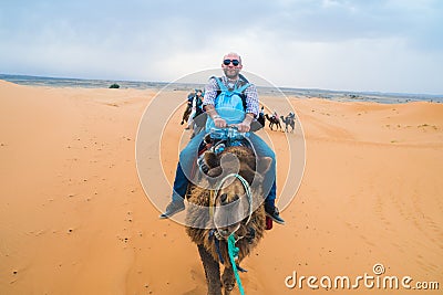Merzouga, Morocco - APRIL 29 2019: Tourist smiling and facing the camera from a camel riding in the Sahara desert tour Editorial Stock Photo