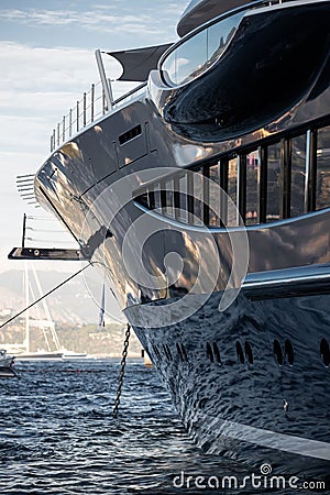 The mesmerizing reflection of the water on the glossy side of a huge yacht anchored, chrome details, chains and ropes to Stock Photo