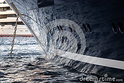 The mesmerizing reflection of the water on the glossy side of a huge yacht anchored, chrome details, chains and ropes to Stock Photo