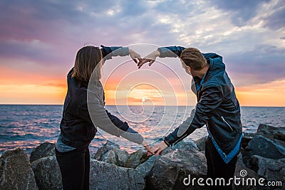 Mesmerizing shot of a loving couple making a heart shape with their arms on the sunset background Stock Photo