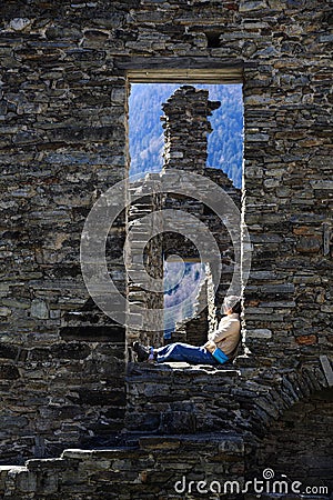 A female visitor sitting on a stone door of the medieaval ruins of Mesocco castle Editorial Stock Photo