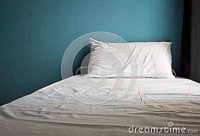 Messy white bed and one pillow , light blue wall Stock Photo