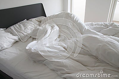 Messy white bedding sheets and pillows with wrinkles on bed in a white bedroom - stock Stock Photo