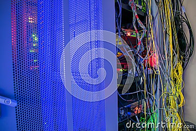 Messy wires are in the switch rack. A bright display glows on the computer equipment in the data center server room Stock Photo