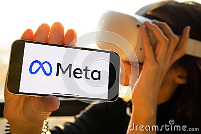 Meta logo on the iPhone, rebranding. Woman holding smartphone with new facebook logo wearing Oculus VR headset. Editorial Stock Photo