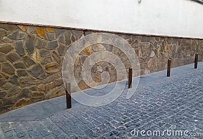 Metal bollards in a cobbled street with stone wall background Stock Photo