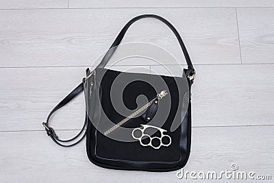 A metal brass knuckles is lying on a black woman`s handbag on a light background. Concept: women`s self-defense, bodily injury, qu Stock Photo