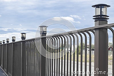 Metal brown fence. There are lamps on poles. Day. Perspective. Stock Photo
