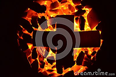 The metal cross lies on the burning coal of a small fraction. Stock Photo