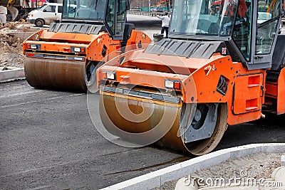 Two large vibratory road rollers compact the fresh asphalt on a new stretch of road Stock Photo