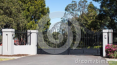 Metal driveway entrance gates set in brick fence with garden trees in background Stock Photo