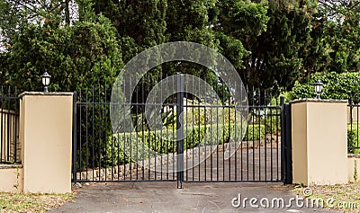 Metal driveway entrance gates set in brick fence with garden trees in background Stock Photo