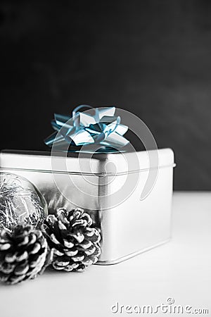 Metal gift box with blue bow and xmas baubles on white and black wooden backgrounds. Stock Photo