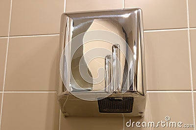 Metal hand dryer on the tiled wall. Hot air for drying hands on the wall with tiles. Drier in public toilet after washing Stock Photo