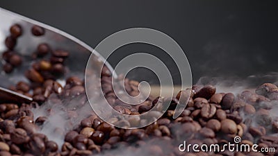 Ladle scooping up coffee beans close up. Light smoke coming over fresh grains. Stock Photo