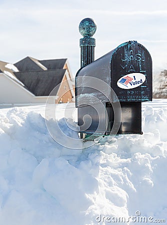 USPS metal mailbox buried in snow drift I voted sticker for vote by mail Stock Photo