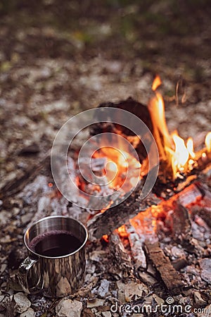 A metal mug with a drink stands next to the fire. Picnic in a camp in the woods. Fireplace in the camp, twilight Stock Photo