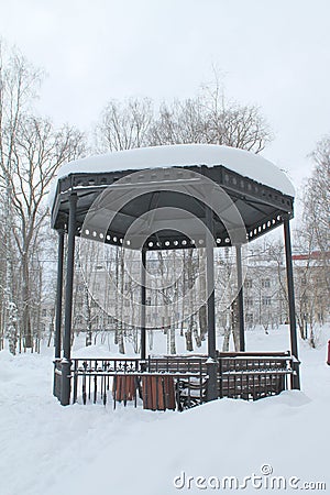 Metal open gazebo with benches in park, covered with snow on cloudy day Stock Photo