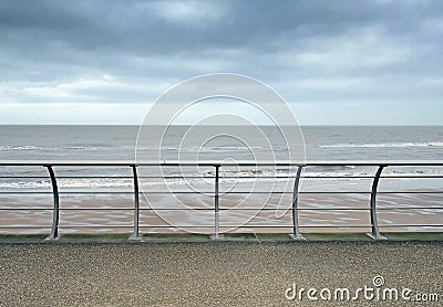 Metal railings on the seafront in blackpool with waves breaking on the beach under a cloudy sky Stock Photo