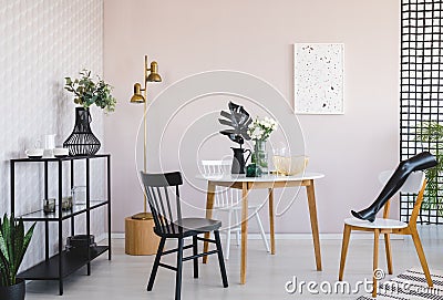 Shelf with plates and glasses in trendy dining room interior with round table with flowers in vase and black leaf in jug Stock Photo