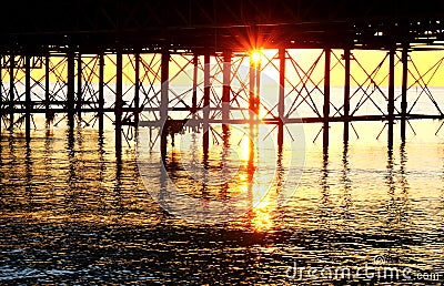 The metal support strutts of Brighton Pier glowing yellow with the sun setting underneath it Stock Photo