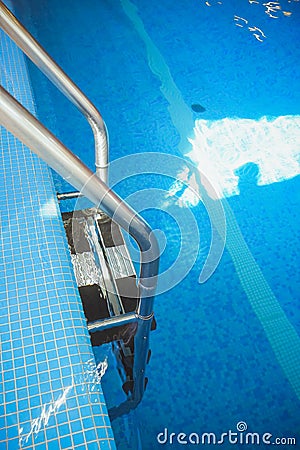 Metal swimming pool steps.Interior of sport hall.Stainless steel swimming pool. hand rails of swimming pool.Ladder in the still Stock Photo