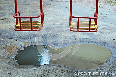 Metal swing with a wooden seat on a kids playground on a rainy day with a puddle under it Stock Photo