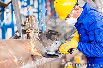 Metal worker in factory grinding metal of pipeline Stock Photo