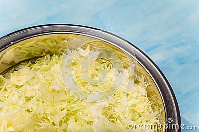 Metallic bowl of cabbage cut into thin strips on blue painted wooden background. Vegetarian, organic, healthy food, diet, Stock Photo