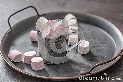 Metallic vintage tray, surface and cup with pink and white marshmallows inside the cup and scattered around the tray Stock Photo