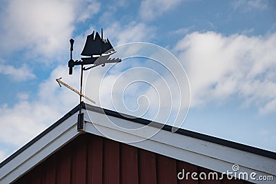 A metallic weather vane on a Scandinavian summerhouse pitched roof resembles an ancient Viking sailing ship or three mast galley Stock Photo