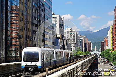 A Metro train travel on elevated rails of Wenhu Line of Taipei MRT System by office towers under blue clear sky Stock Photo