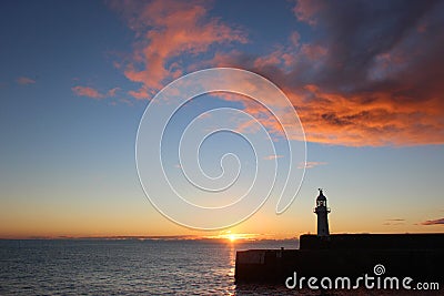 Mevagissey lighthouse at sunrise beneath red tinted clouds. Sun leaves a bright path over the sea. South coast, Cornwall UK Stock Photo