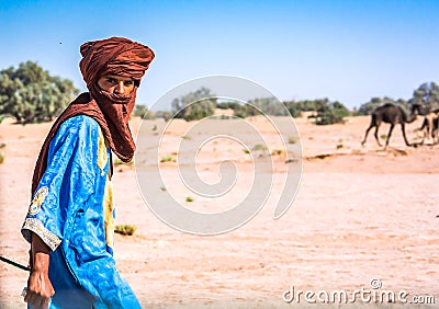MHamid, Morocco - October 10, 2013. Young berber walking on desert Sahara in traditional clothes with loaded camels Editorial Stock Photo