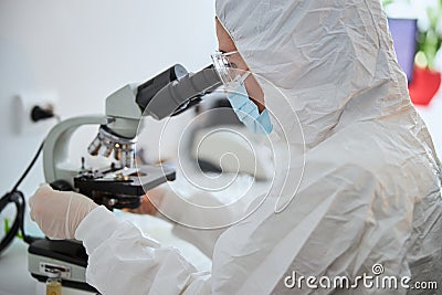 Microbiologist in a hazmat suit observing a microscopic specimen Stock Photo