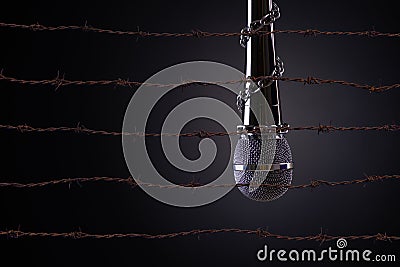 Microphone with a chain and rusty sharp bare wire, depicting the idea of freedom of the press or expression on dark background. Stock Photo