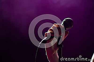 Microphone in hand singer on stage. Live music background. Microphone and stage lights. Stock Photo