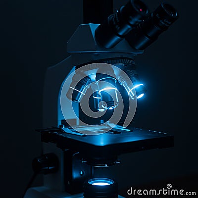 A microscope with multiple objective lenses, illuminated by a blue light, creating Stock Photo