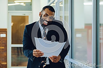 Mid adult bearded black man Entrepreneur Businessman wearing suit holding papers and talking on smartphone laughing Stock Photo